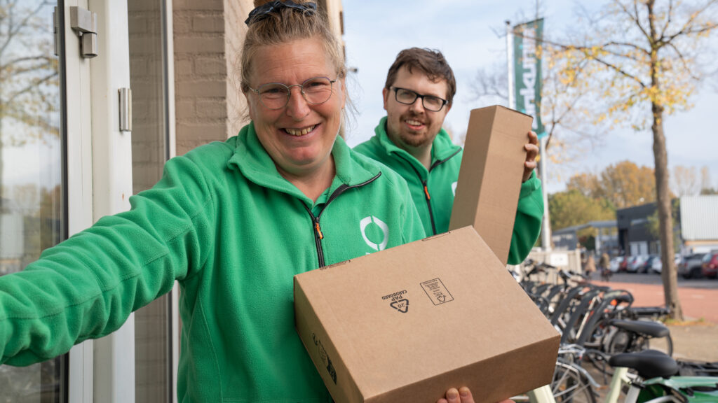 Twee medewerkers van Ergon Post staan met pakketten bij een deur.