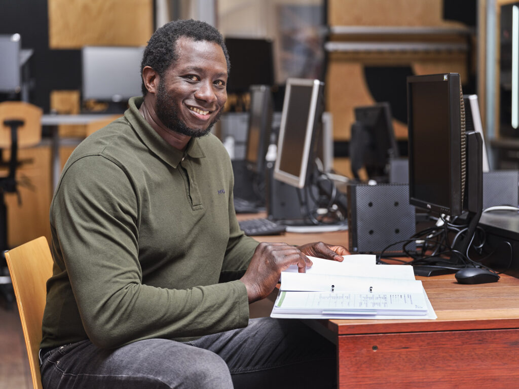 Een Trajectcoach leest een handleiding aan een bureau en lacht in de camera.