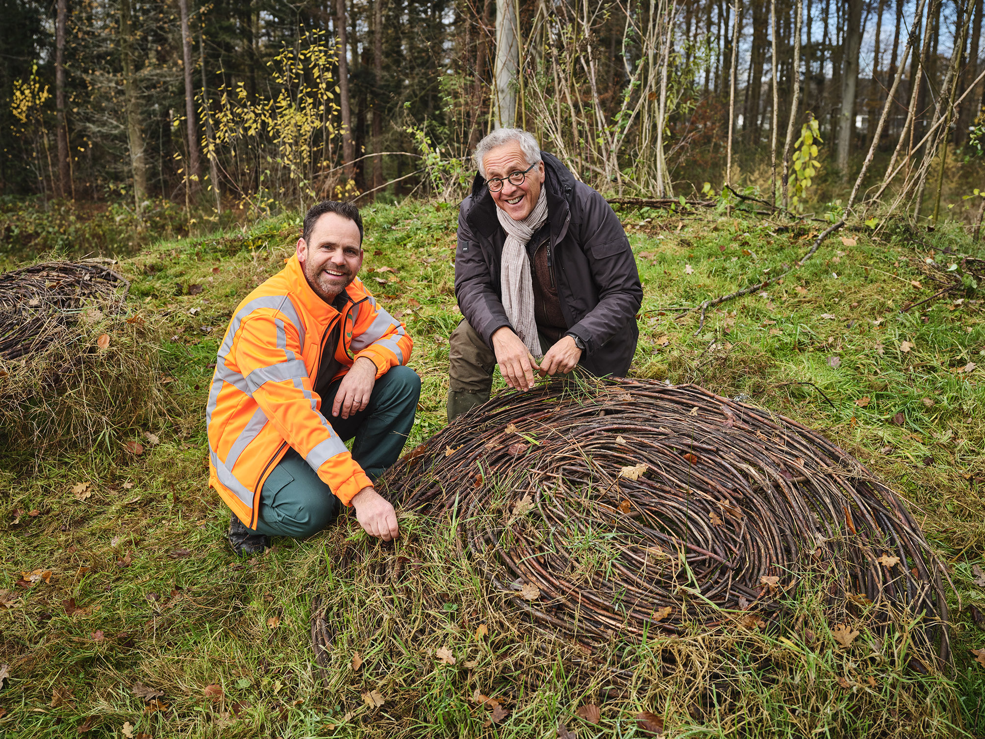 Een medewerker van Ergon Groen zit met een klant gehurkt in gesprek bij een natuurlijk kunstwerk.